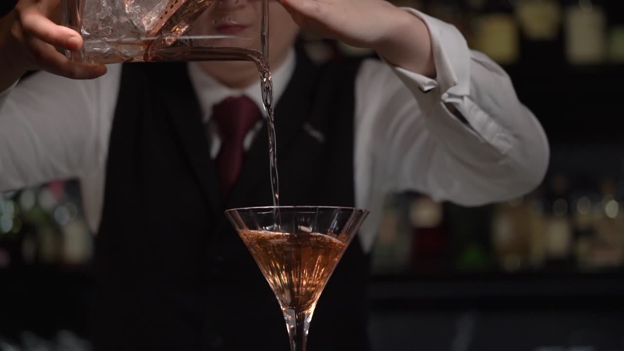 Una giovane barista versa elegantemente il martini freddo leggermente diluito in un bicchiere da cocktail usando un colino di rame e un mixing glass di cristallo.