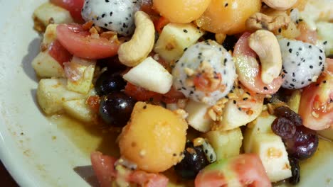 close up footage of thai style mix exotic fruits somtum with sweet and salty dressing included dragon fruit, cashew nut, grape, guava, melon and tomato