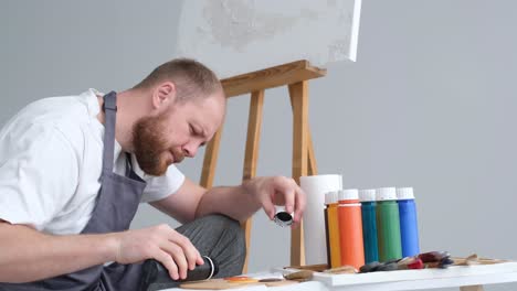 a professional artist mixes a palette of paints for painting - a professional artist mixes a palette of paints for painting. behind him is an easel with a white canvas. young male artist paints a picture in the studio