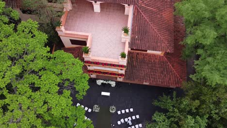 wedding ceremony set-up, green trees contrast with red house, aerial top-down