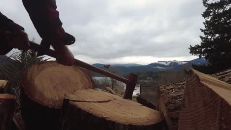 close up slow motion of axe hitting log round with pieces flying with lake and mountains in background