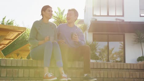 video of happy diverse couple talking and drinking coffee in garden