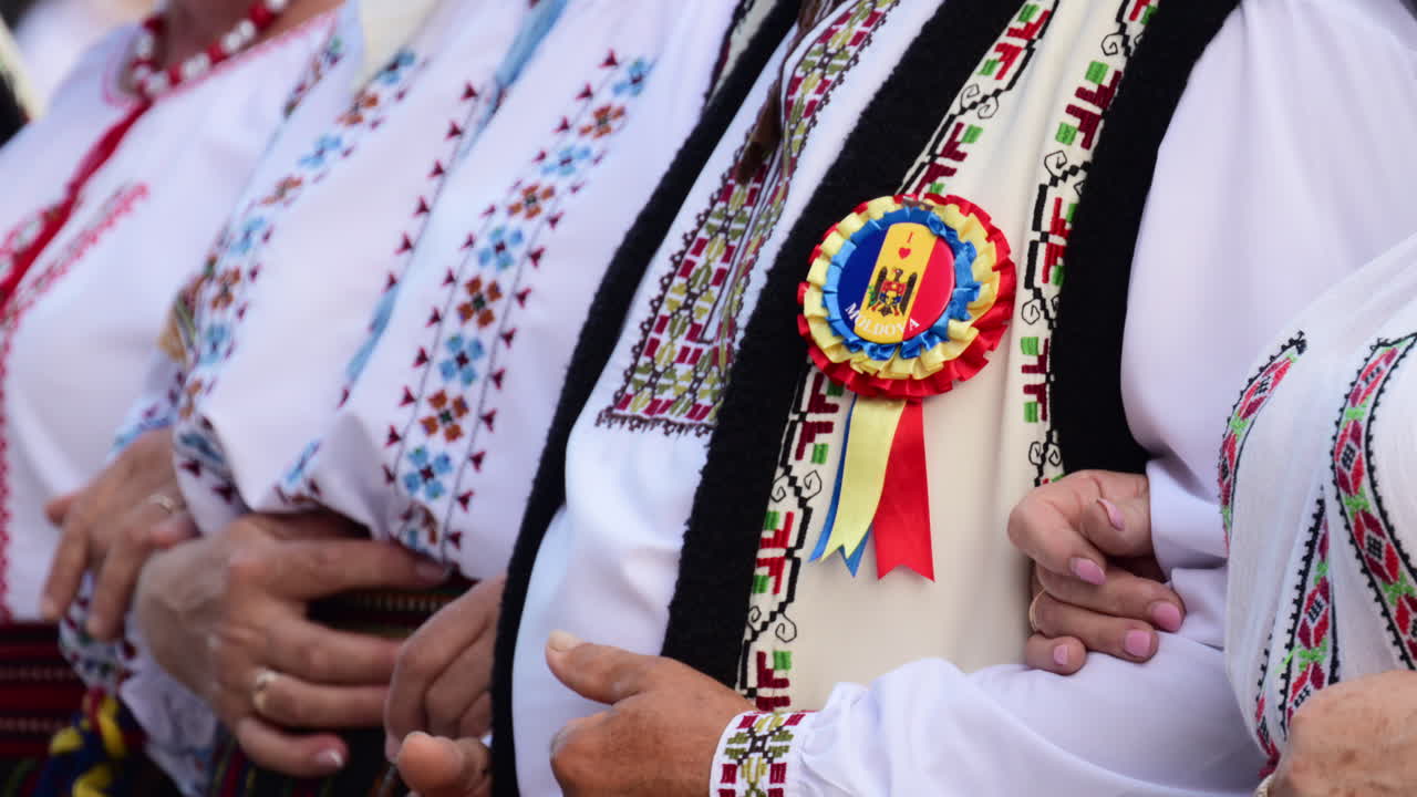 People dressed in colorful traditional clothing stand together, celebrating their cultural heritage at a folk event in Chisinau. Man wearing I Love Moldova sign