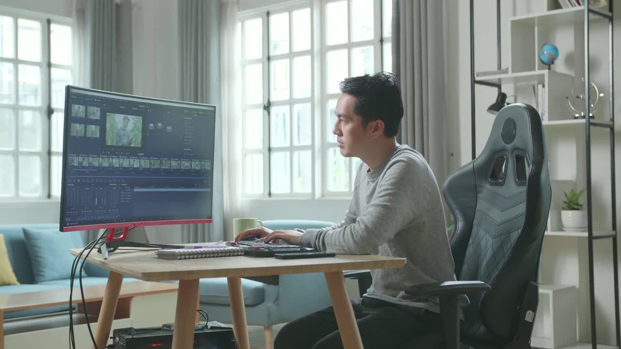 Asian Video Editor Man In Long Sleeved T-Shirt And Black Pants Using Desktop Computer For Editing Video While Working At Home.
