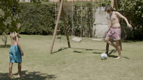 niños caucásicos felices jugando a la pelota en el césped en un día de verano