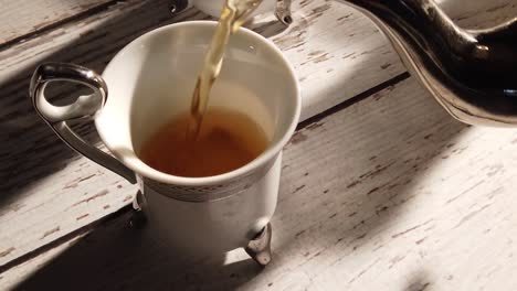 slow motion extreme closeup of tea pouring into a turkish cup on a distressed wood table