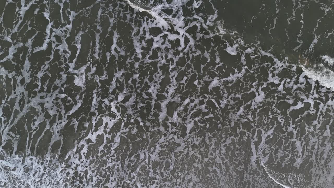 White foamy sea waves crashing against the seandy beach aerial view