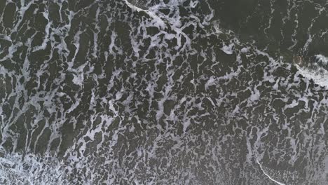 white foamy sea waves crashing against the seandy beach aerial view