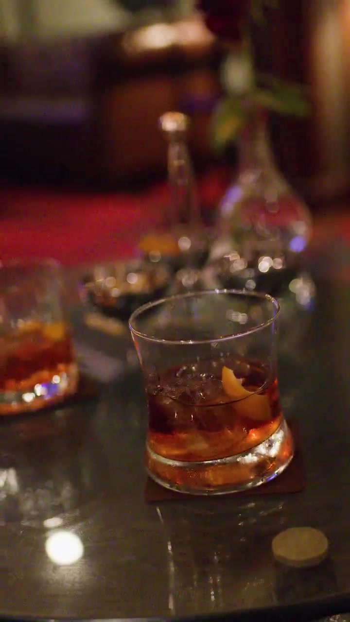 Bicchiere di whisky con ghiaccio e scorza d'arancia, illuminazione soffusa del bar, profondità di campo ridotta