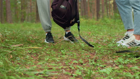 close up ground level view of two people standing still in forest with visible sneakers a as they pause during walk, drop bag on forest floor and prepare to take short rest among trees