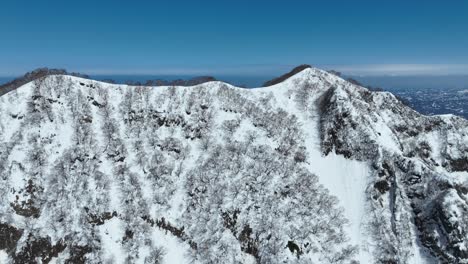 aerial fly over shot of top of myoko mountain summit, japans coast line and ocean sea visible in background