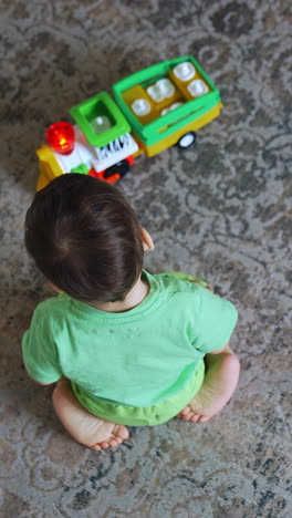 active dark-haired toddler crawls by the carpet. kid plays with a toy car. top view. vertical video