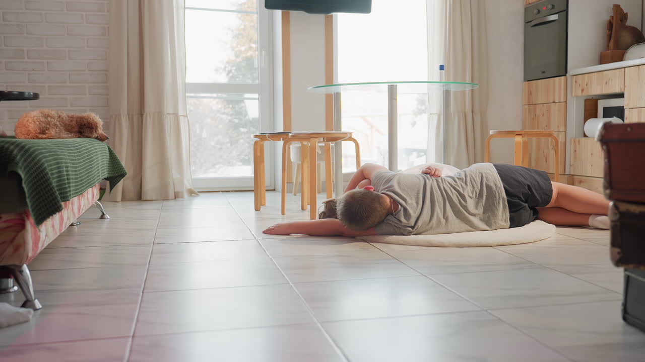 Partial view of woman's legs in white socks sitting with dog on couch, while boy and girl lie on white rug facing each other, background shows television, chairs, and television stand in cozy room