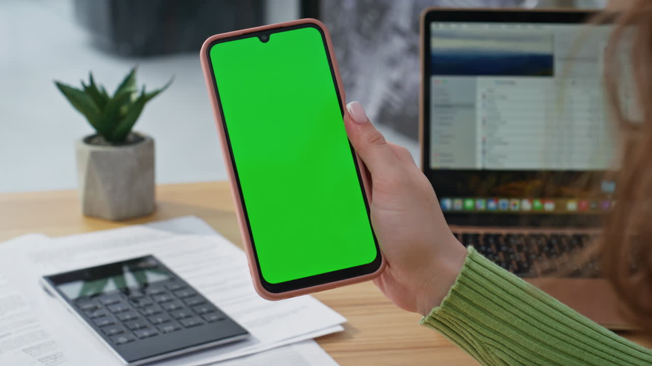 Closeup hand holding mockup cellphone in office. Woman watching green screen