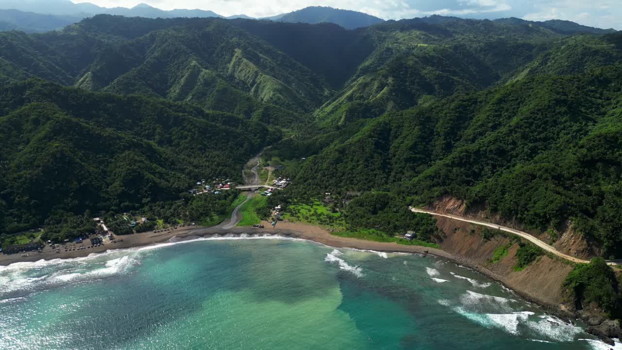 Slow zoom drone shot of the lush green hills in Matawe, Dingalan, Aurora, revealing slopes rising above the coastline, with turquoise waters and waves framing the dramatic landscape