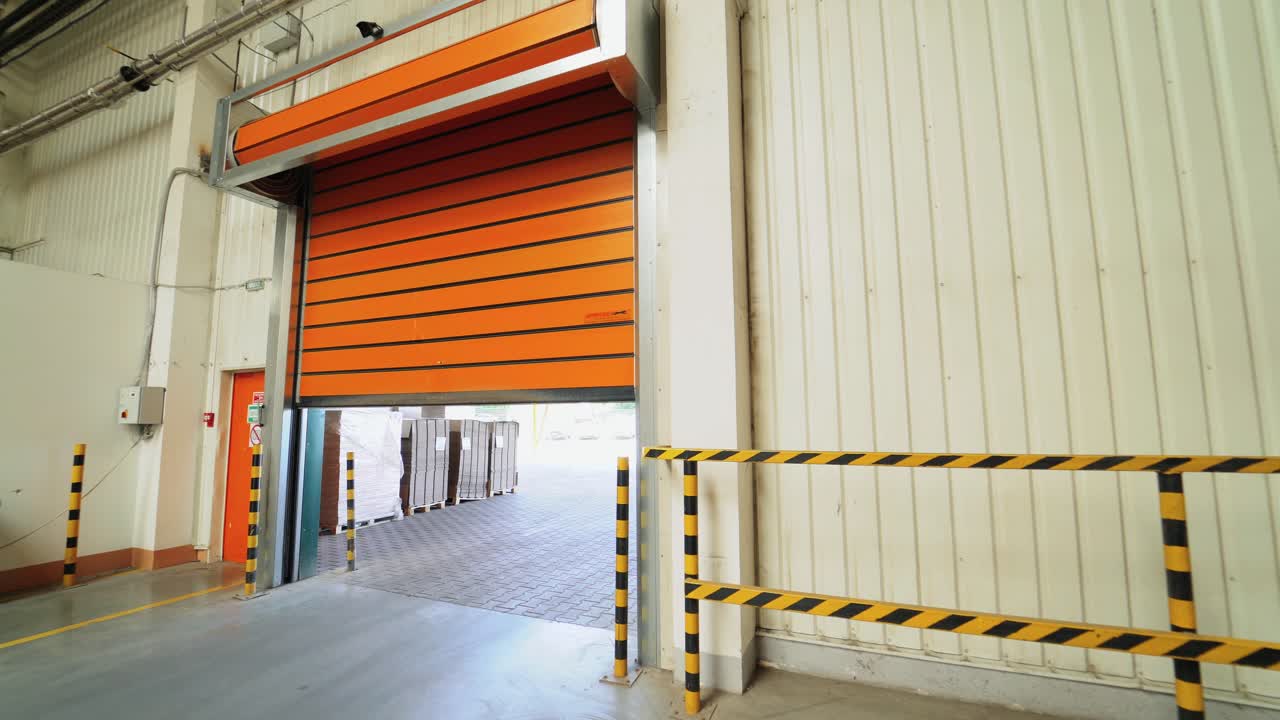 automatic roller gates of orange color are lowering down in the warehouse of woodworking plant. Camera movement to the right