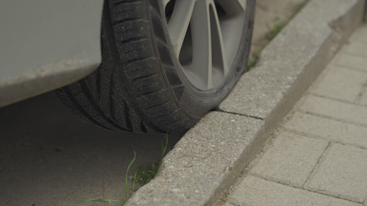 Primo piano di un'auto parcheggiata male con la ruota sul marciapiede.