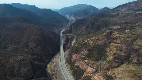 Panoramic-road-passing-through-river-valley-of-high-mountains-in-Albania,-aerial-view-of-highway