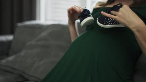 unrecognizable woman walking baby shoes on her pregnant belly at home on sofa