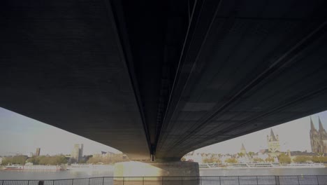 tilt down shot from under a bridge that is dark to reveal the river and cityscape with old church steeples and modern buildings one a sunny clear day