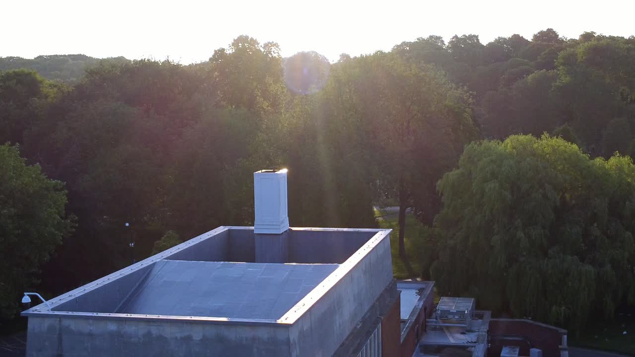Golden hour sunrise aerial view descending over woodland crematorium rooftop with sunlit rays