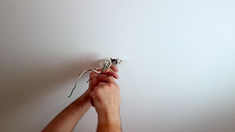 Fasten-a-screw-on-a-ceiling-light-mount-with-wires-hanging-from-a-hole