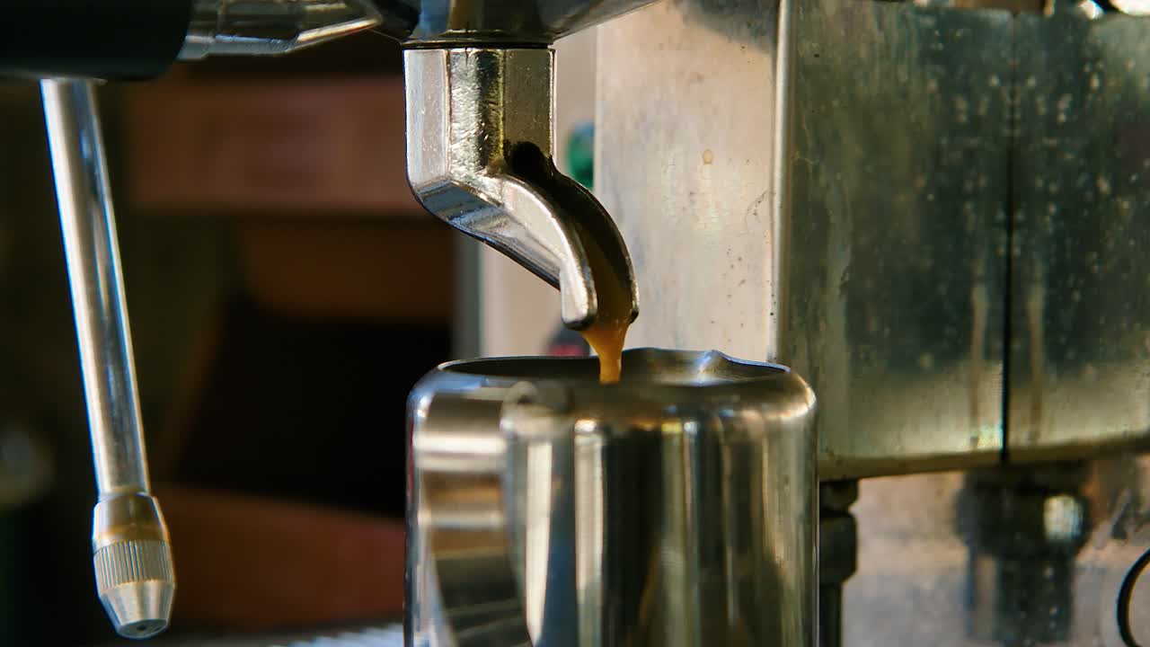 Closeup orbit of coffee dripping out into metal tea cup in slow motion