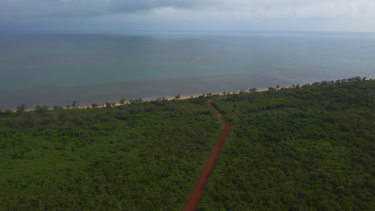 un dron captura una vista impresionante de un camino de tierra roja que serpentea a través de una densa vegetación tropical y conduce a una playa impresionante y una laguna azul cristalina
