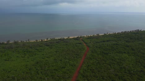 Un-Dron-Captura-Una-Vista-Impresionante-De-Un-Camino-De-Tierra-Roja-Que-Serpentea-A-Través-De-Una-Densa-Vegetación-Tropical-Y-Conduce-A-Una-Playa-Impresionante-Y-Una-Laguna-Azul-Cristalina