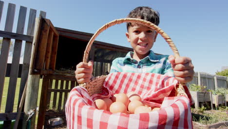 Retrato-De-Un-Niño-Birracial-Feliz-Sosteniendo-Una-Canasta-Con-Huevos-Al-Lado-Del-Gallinero,-Cámara-Lenta