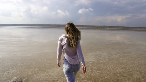 joyful woman in casual is running on sandy shallow of lake at summer