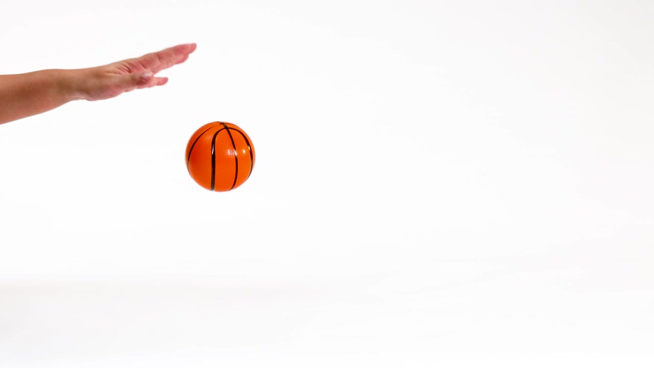 A hand dribbles and catches a small orange toy basketball against a plain white background