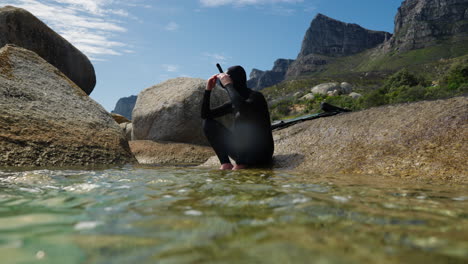 free diver sitting on a rock on the edge of crystal clear ocean water