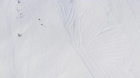 toma aérea de arriba hacia abajo de dos personas caminando por un camino nevado que sube la montaña