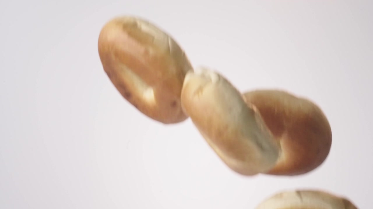 Bagel dorati e gommosi che piovono su uno sfondo bianco senza soluzione di continuità al rallentatore cinematografico. Contenuti per gastronomia newyorkese, branding per negozio di bagel, reel per menu brunch