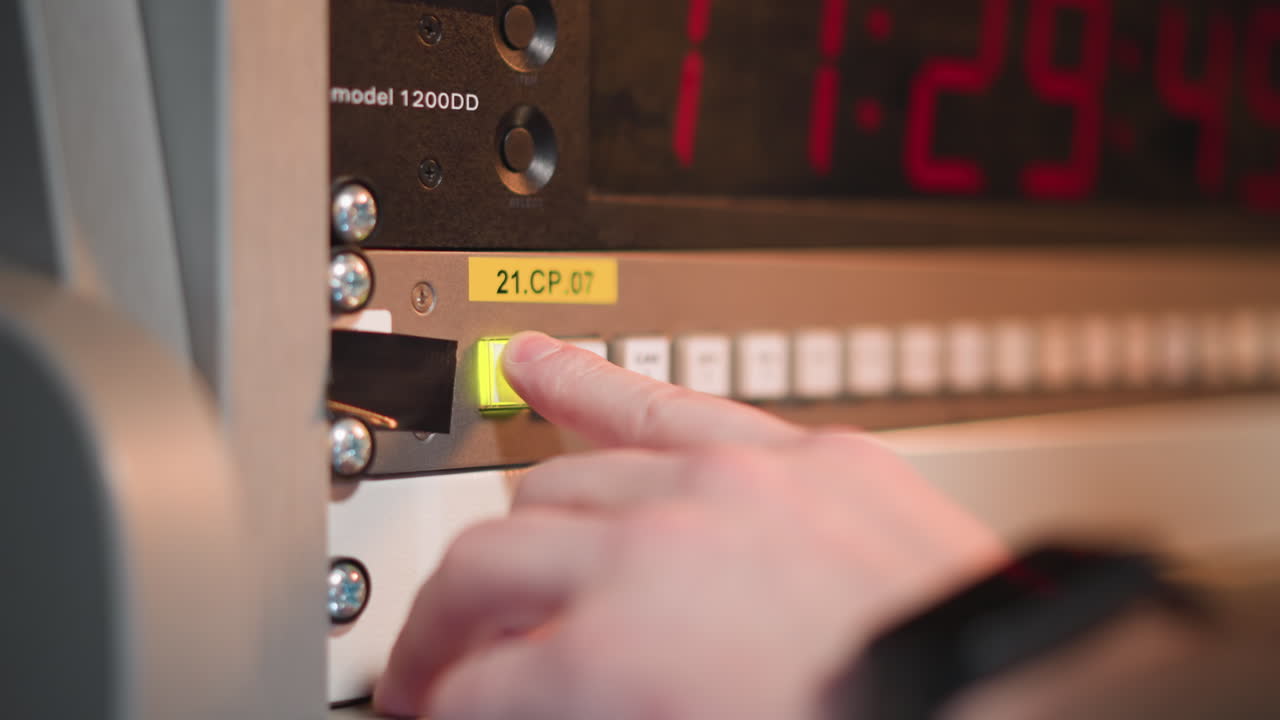 Close-up shot of finger pressing green button on control panel, with large red timer display in background. Professional video production or broadcast control system in action