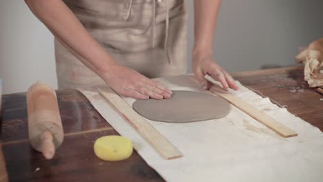 artist is unrolling clay on table in workshop, using pin, close-up of hands