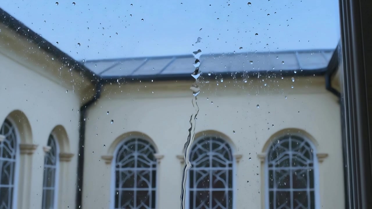 Joining droplets on window glass forming, sliding water streak from rain at courtyard with windows