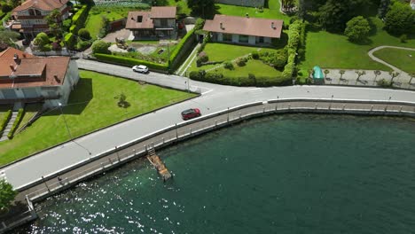 an aerial view of a serene residential neighborhood featuring houses with lush gardens, a winding road, and a tranquil waterfront, capturing a peaceful suburban lifestyle