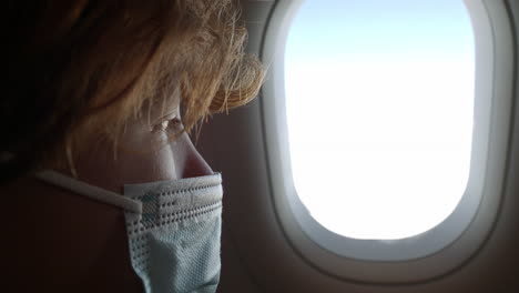 niño con máscara mirando por la ventana del avión