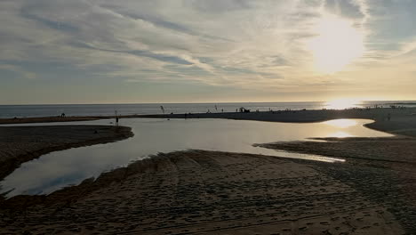 Pequeño-Lago-De-Agua-Formado-En-La-Playa,-Después-De-La-Marea-Alta,-Al-Fondo-El-Mar-Y-El-Sol-Poniente