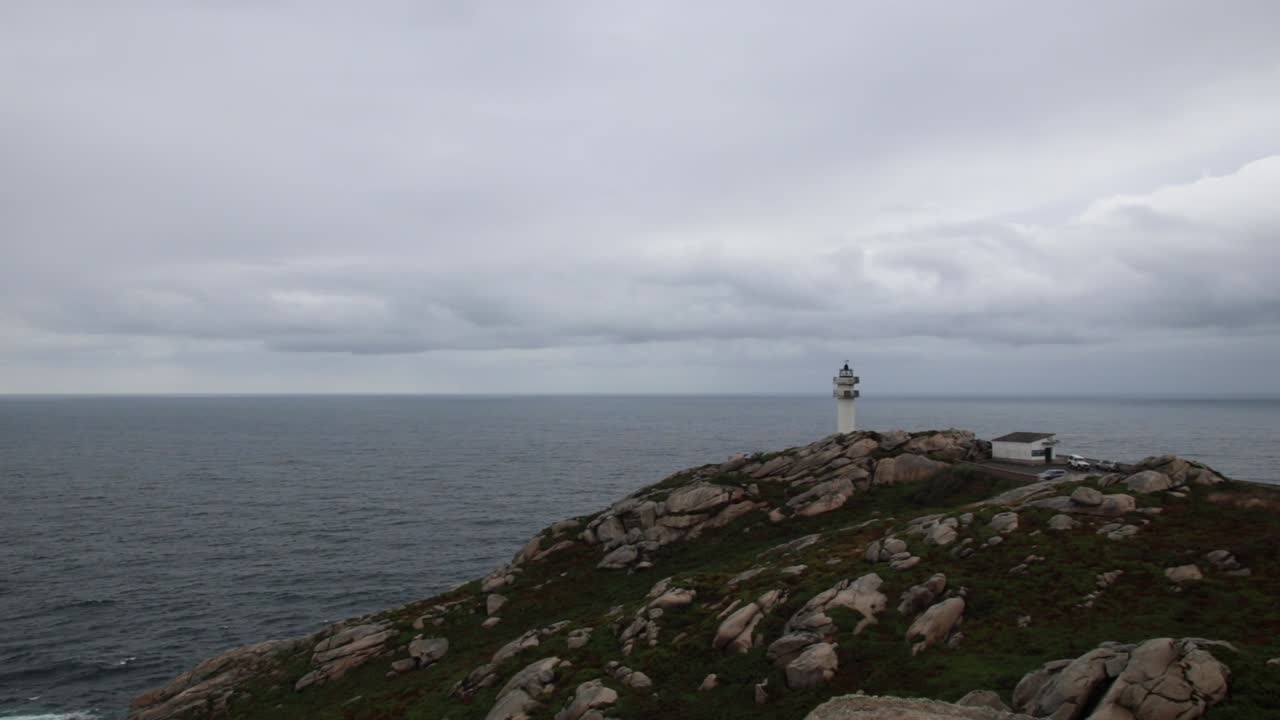 White lighthouse stands atop rocky green hill beside scattered coastal homes, overlooking wide sea and cloudy sky, quiet atmosphere at St Ives Cornwall with rugged landscape and calm water