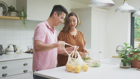 asian couple unpack fresh and healthy local food in zero waste packaging from bag in kitchen at home