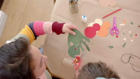 madre y hija bi-raciales felices cortando recortes en la sala de estar soleada