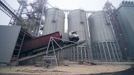 high-lifted car full of grain at the agricultural factory. unloading grain into the bunker of granary. circle view at the car against the silver tanks.
