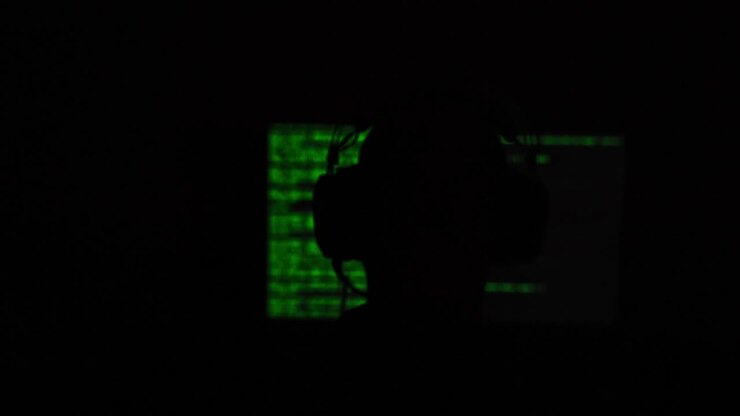 Hacker zittend voor een computerscherm met groene code in een donkere, schimmige kamer. Vervaagd scherm.