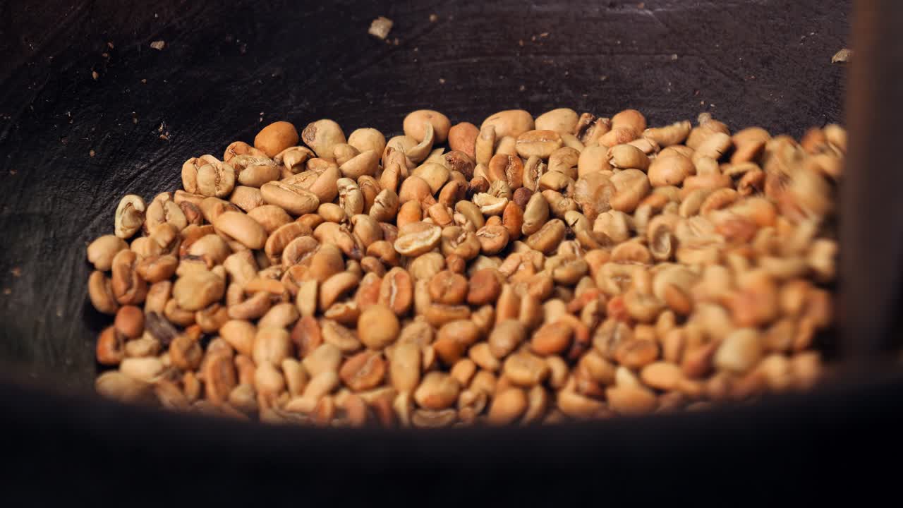 Close up slow motion shot of roasted coffee beans kopi luwak while the beans are stirred and roasted in a wok with a wooden spoon in Bali, indonesia