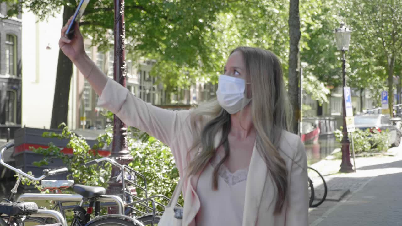 una mujer viajera feliz tomando selfie mientras camina por una carretera pavimentada cerca del canal de amsterdam en países bajos