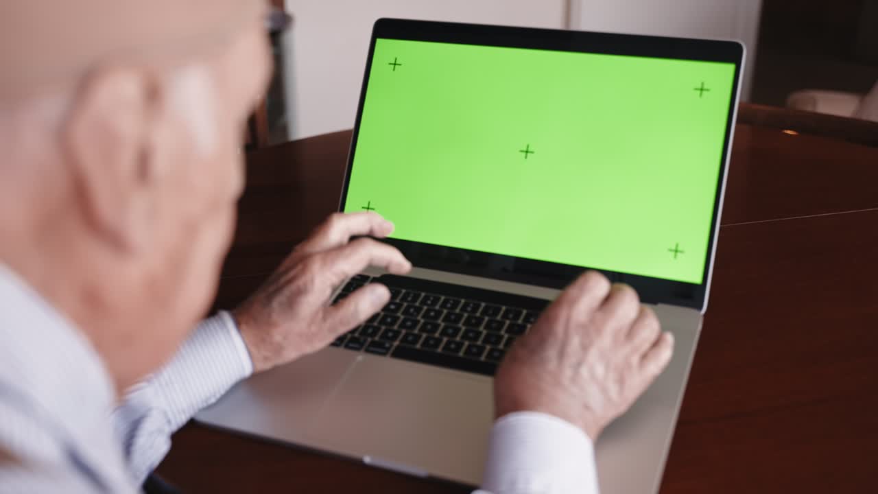 pensionista sentado en la mesa y trabajando en una computadora portátil de moda con pantalla verde tecla de croma, manos de anciano escribiendo en el teclado de la computadora