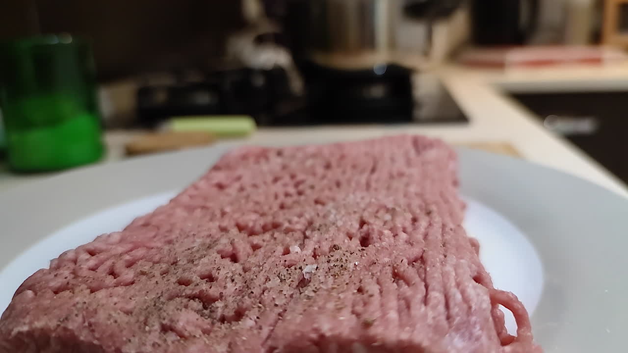 carne molida con pimienta y sal en una placa blanca lista para cocinar en la cocina